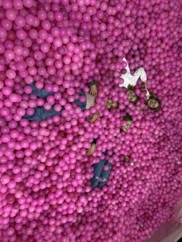 Girls peeking out of a pink ball pit