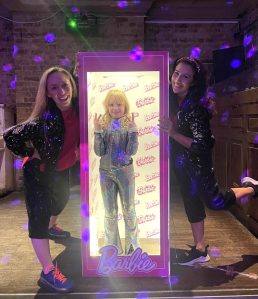 Two dancers posing next to a girl in a glowing Barbie frame
